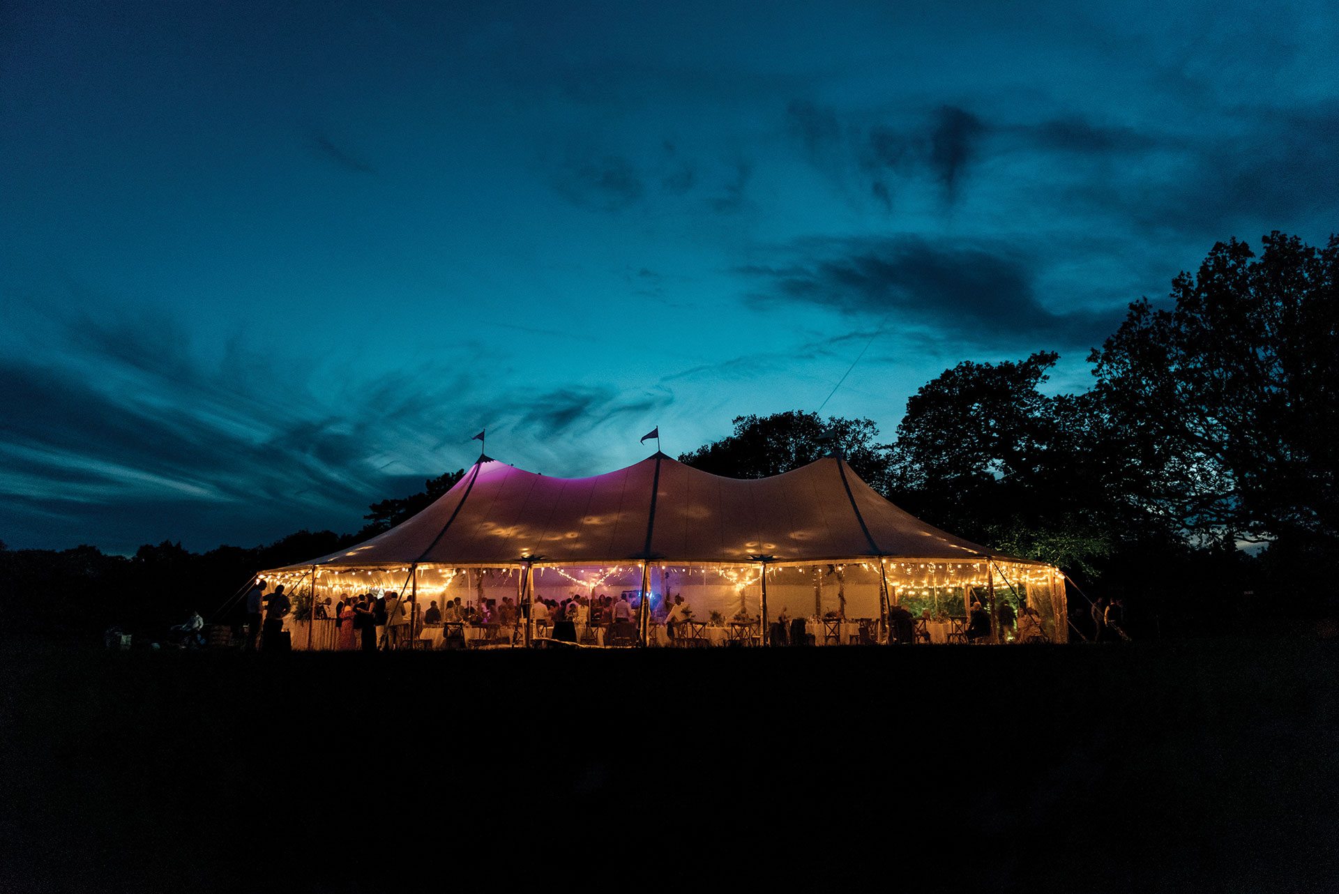 Dark blue sky background lit up tipi/tent with people and seating
