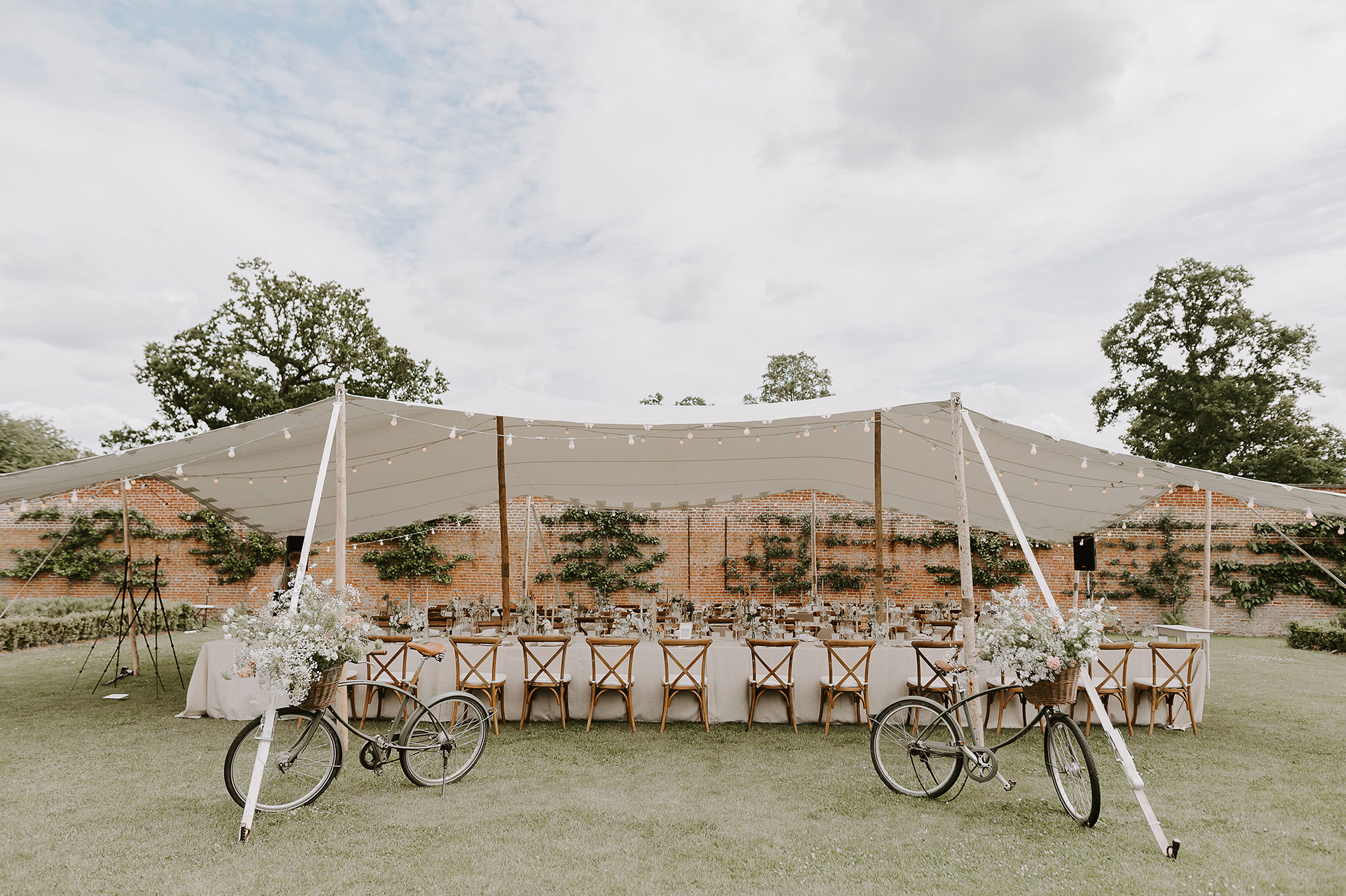 10 x 15 Stretch Tent Pretty Lifestyle shot with cross back chairs, festoon lights and floral arrangements