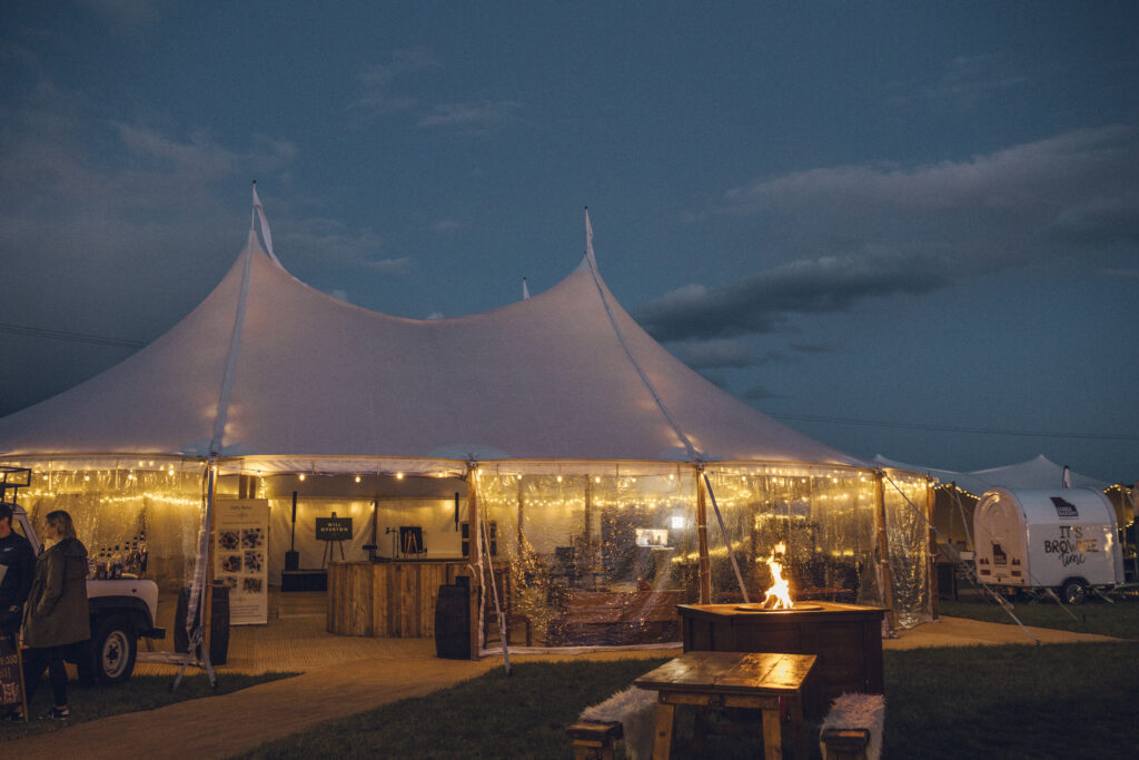 Sailcoth tent at night with sides down and firepit outside with festoon lights in the Sailcloth tent