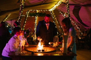 family around a firepit inside a tipi for a wedding cooking marshmellows
