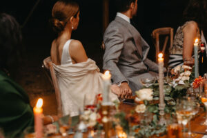 Bride and groom hold hands at their top table during their wedding ceremony inside a marquee