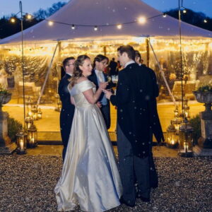 Bride and groom outside a sailcloth marquee lit with festoon lights in light winter